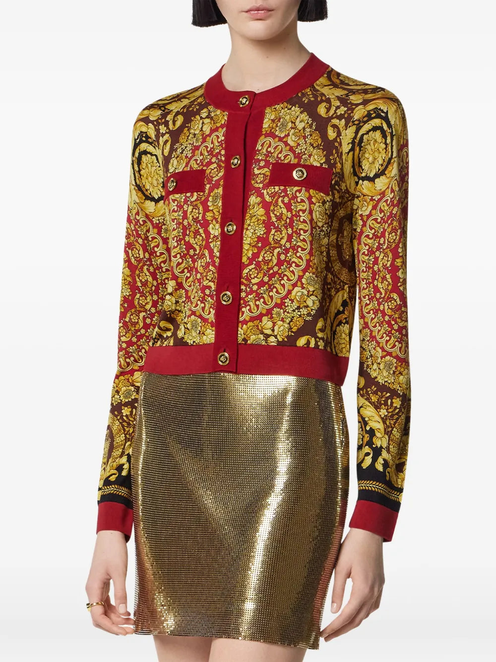 Woman wearing a Versace barocco cardigan with red and gold accents and a gold skirt.