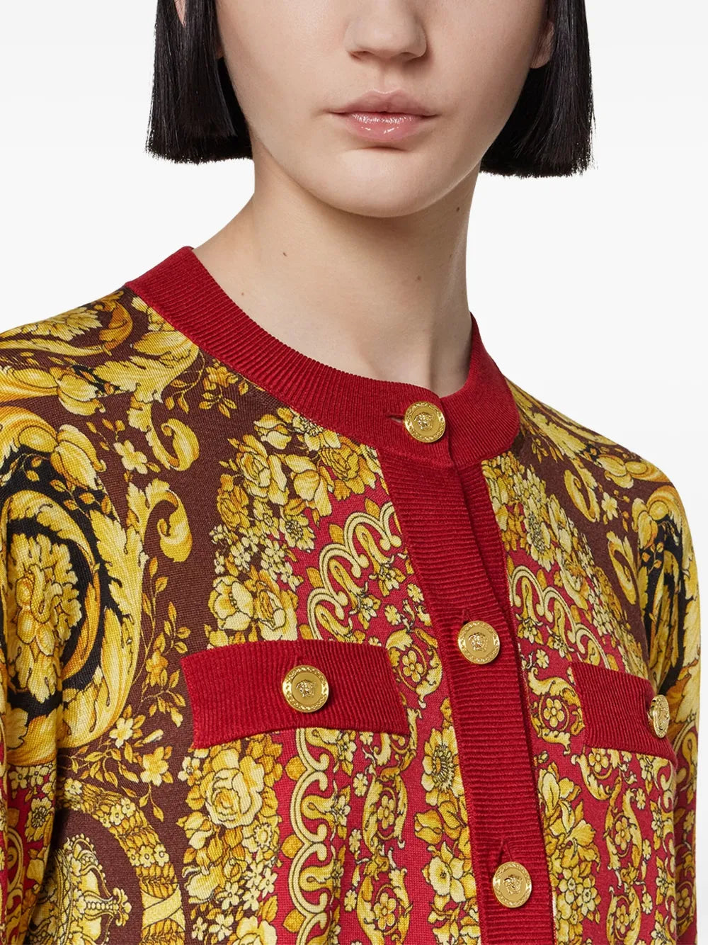 Woman wearing a red and gold barocco design cardigan.