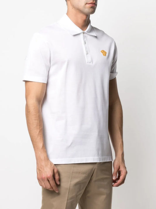 Model wearing a white polo shirt with a gold medusa on the chest.