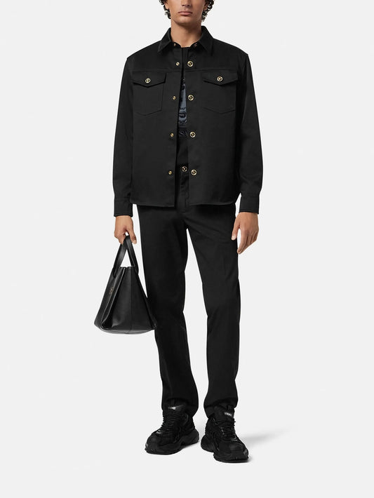 Man wearing a black jacket, pants, and shoes holding a black bag on a white background