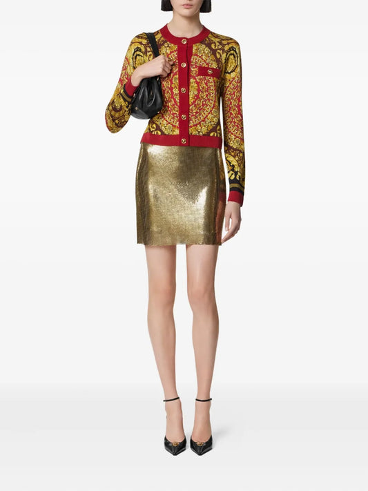Woman wearing a VERSACE barocco cardigan sweater and gold skirt on a white background