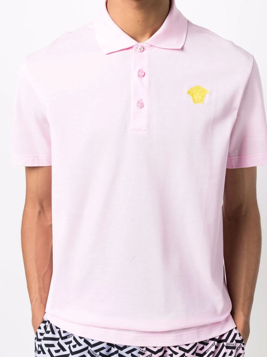 Model wearing a pink polo shirt with a gold medusa logo.