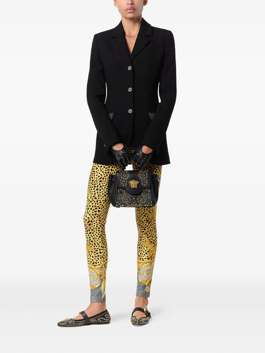 Model wearing leopard print leggings and holding a black handbag with gold, silver and black embellishments on a white background.