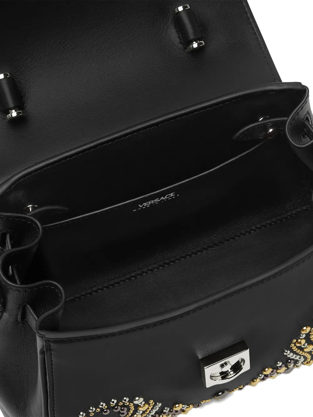 Interior shot of a handbag with gold, silver and black embellishments on a white background.